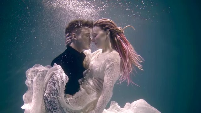 Side view shot of a stunning couple of a lovers floating underwater hugging.
