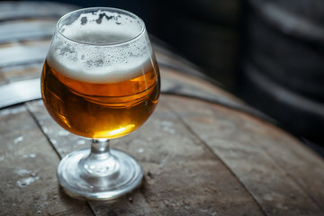 Snifter beer glass on a wooden barrel