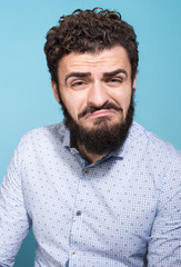 Obraz premium Studio portrait of unhappy young man with a grimace on his face. Beard, mustache and a light shirt