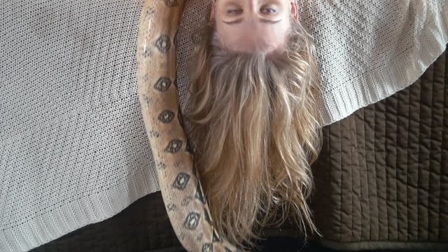 Python crawling on the body of young smiling female dancer on the bed