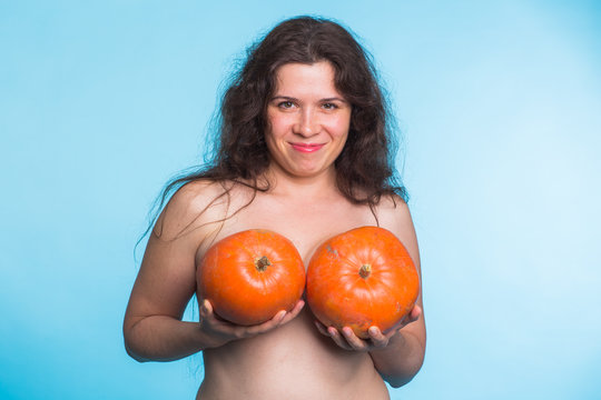 Young happy woman holds pumpkin in hands above her breast. Plastic surgery and silicone implants concept.