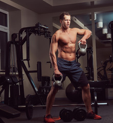 Fototapeta premium Handsome muscular shirtless bodybuilder male doing exercises with a dumbbell in the gym.