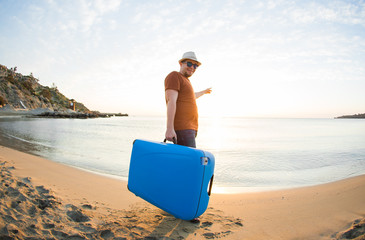 Man holding suitcase and points on the sea. Travel concept.