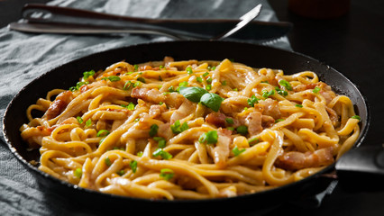 Close up of cooking traditional Italian pasta Carbonara in a frying pan on dark wooden background