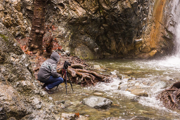 Young photographer with backpack making photos of waterfall and rocks with the camera. Mediterranean sea