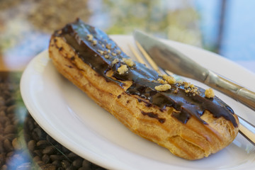 .Traditional French eclairs with chocolate and nuts on a white plate.