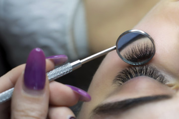thick lashes in front of the girl and in a round mirror on a stick in the hands of the master