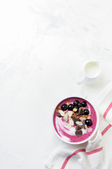 Pink black currant berries, banana smoothie bowl with granola, flakes from almonds and chocolate on light gray concrete background. Selective focus. Top view. Copy space.