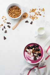Pink black currant berries, banana smoothie bowl with granola, flakes from almonds and chocolate on light gray concrete background. Selective focus. Top view. Copy space.