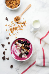 Pink black currant berries, banana smoothie bowl with granola, flakes from almonds and chocolate on light gray concrete background. Selective focus. Top view. Copy space.