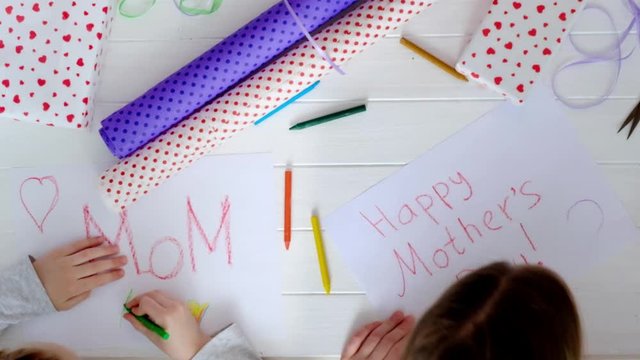 Little girl drawing happy mother's day greeting card with presents on the table