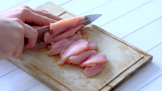 hands cutting chicken meat into pieces. Hand slicing raw fillets for cooking with knife on wooden cooking board
