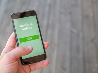 Order fast food online on a smart phone app. Home delivery. Wood background.