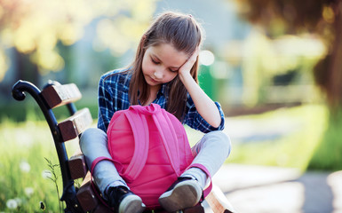 Unhappy schoolgirl sitting in the park. Education, lifestyle concept