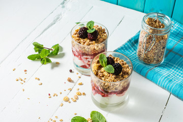 Healthy layered dessert with yogurt, granola, jam, blackberry in glass on wood background