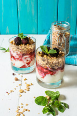 Healthy layered dessert with yogurt, granola, jam, blackberry in glass on wood background