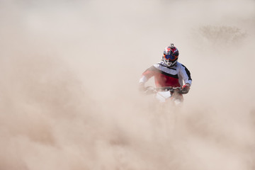Motocross rider racing in a large cloud of dust and debris