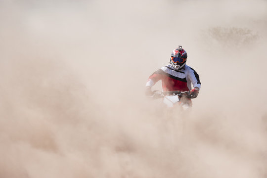 Motocross rider racing in a large cloud of dust and debris