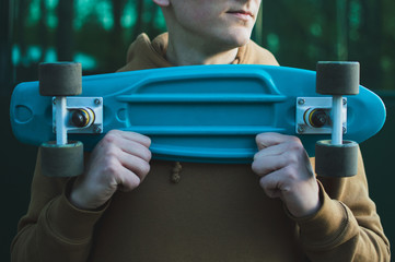 Young hipster man in the brown hoodie holding blue plastic skateboard in horizontal position on the...