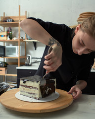 Step-by-step preparation of black designer cake. The confectioner is applying a black frosting on the cake.