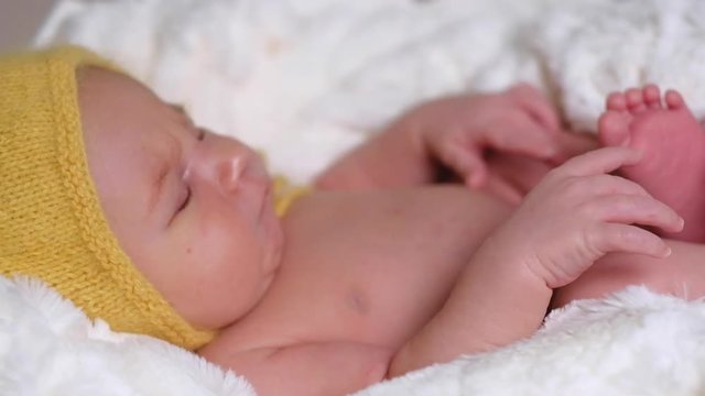 Lovely newborn child in yellow hat sleeping on white soft blanket