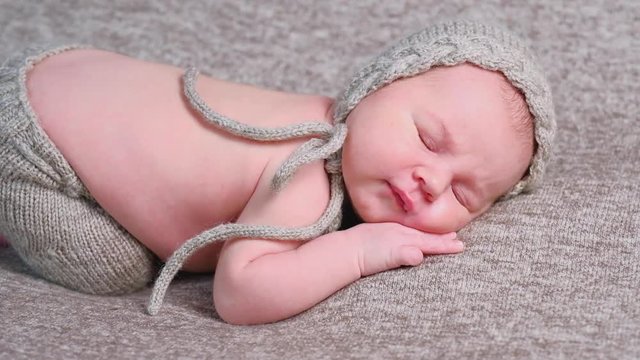 Cute sleeping newborn child in brown bonnet asleeps on soft blanket