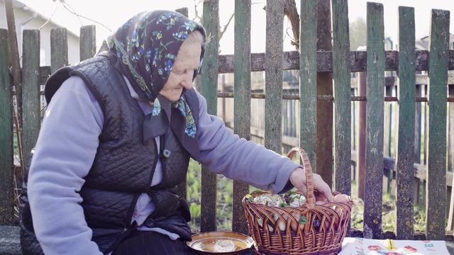 Easter holiday in the Ukrainian village - the old authentic grandmother preparing the Easter basket on the bench in the courtyard.