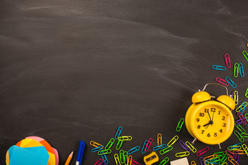 bright office supplies, yellow alarm clock on black chalkboard top view, copy space. concept: back to school, school's out, school holidays, teacher's day