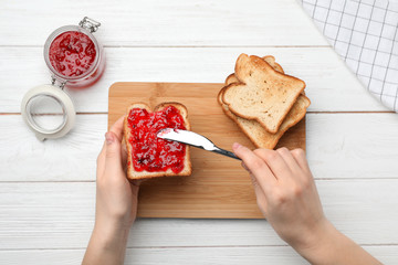 Woman spreading jam on toast against wooden background