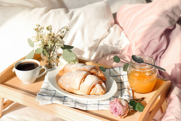 Tray with delicious croissants, cup of coffee and honey on bed