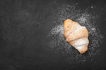 Tasty croissant with sugar powder on dark background, top view