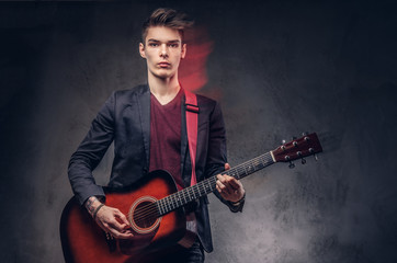 Obraz premium Stylish young musician with stylish hair in elegant clothes, playing on an acoustic guitar.