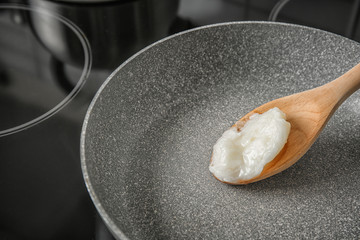 Wooden spoon with coconut oil in frying pan. Healthy cooking