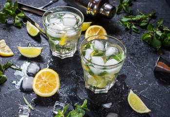 two glass of mojito cocktail with fresh lime and mint on a black stone board