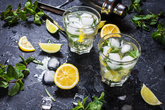 two glass of mojito cocktail with fresh lime and mint on a black stone board