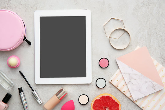 Flat lay composition with tablet and makeup products on grey background