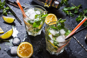 two glass of mojito cocktail with fresh lime and mint on a black stone board