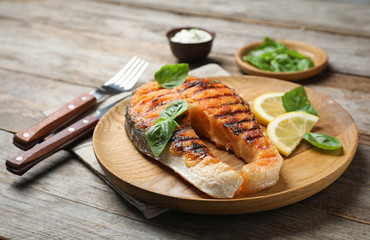 Plate with tasty salmon steak on wooden table