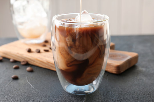 Pouring milk into glass with cold brew coffee on table