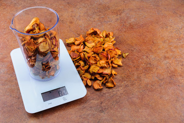 Dried apples in a measuring cup on electronic scales with a copy space. The ratio of product volume to its weight.