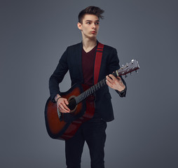 Obraz premium Handsome young musician with stylish hair in elegant clothes, playing on an acoustic guitar.