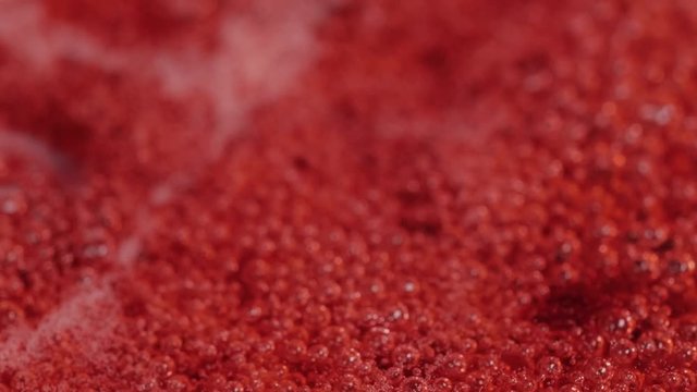 Bubbles rising in thick, red liquid making an abstract background. Macro shot of a cranberry jam.
