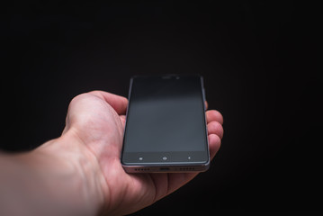 Hand holding black smartphone isolated on black background