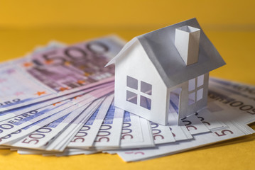Small paper house on pile of money closeup. Real estate price concept. Selective focus