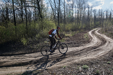 A young man in sports clothes rides a bicycle on the road in the forest.