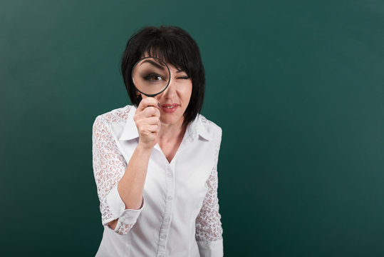 a woman looks forward through a magnifying glass, a blackboard as a background, big eye is visible inside the magnifier, a concept of education and business