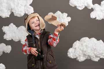 boy dressed as an airplane pilot stands between the clouds and playing with handmade plane