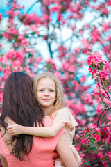 Adorable little girl with young mother in blooming cherry garden on spring day