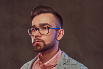 Close-up portrait of a confident stylish bearded man with hairstyle and glasses in a gray suit and pink shirt, posing in a studio.