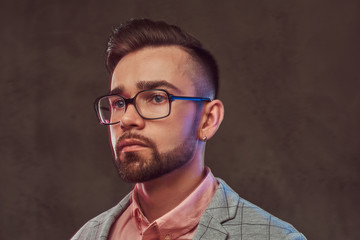 Close-up portrait of a confident stylish bearded man with hairstyle and glasses in a gray suit and pink shirt, posing in a studio.